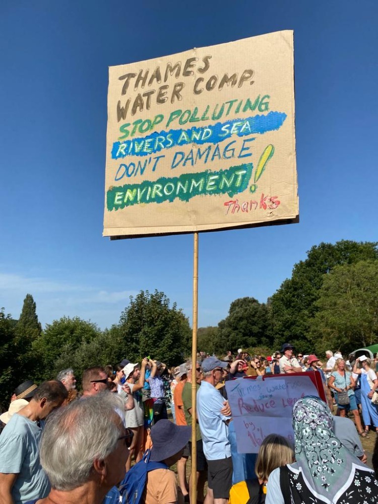 Save Ham Lands and River group holding up a sign that reads "Thames Water Comp. Stop polluting rivers and sea. Don't damage our environment! Thanks" in protest against Thames Water