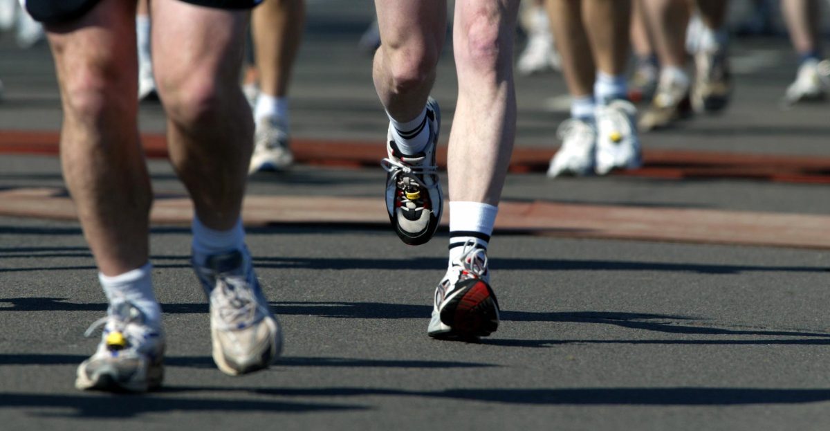 A frontal shot of the shoe and legs of white, male marathon runners on pavement. 