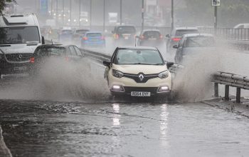 A white car driving on a flooded road. Water splashing at the sides of the car.