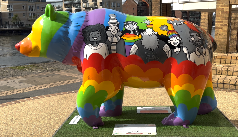A bear sculpture painted with Pride rainbow colours and a diverse collection of illustrations of people.