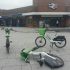 Three Lime bikes parked in the middle of the pavement in front of Kingston Station. One bike has fallen on the floor.